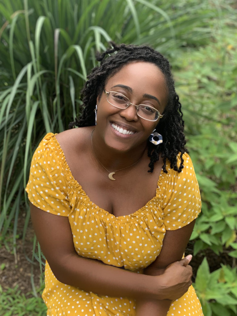 Herbalist Referrals 8 headshot of christina lynch taken at a downward angle with her wearing a yellow dress, and surrounded by green grassy background